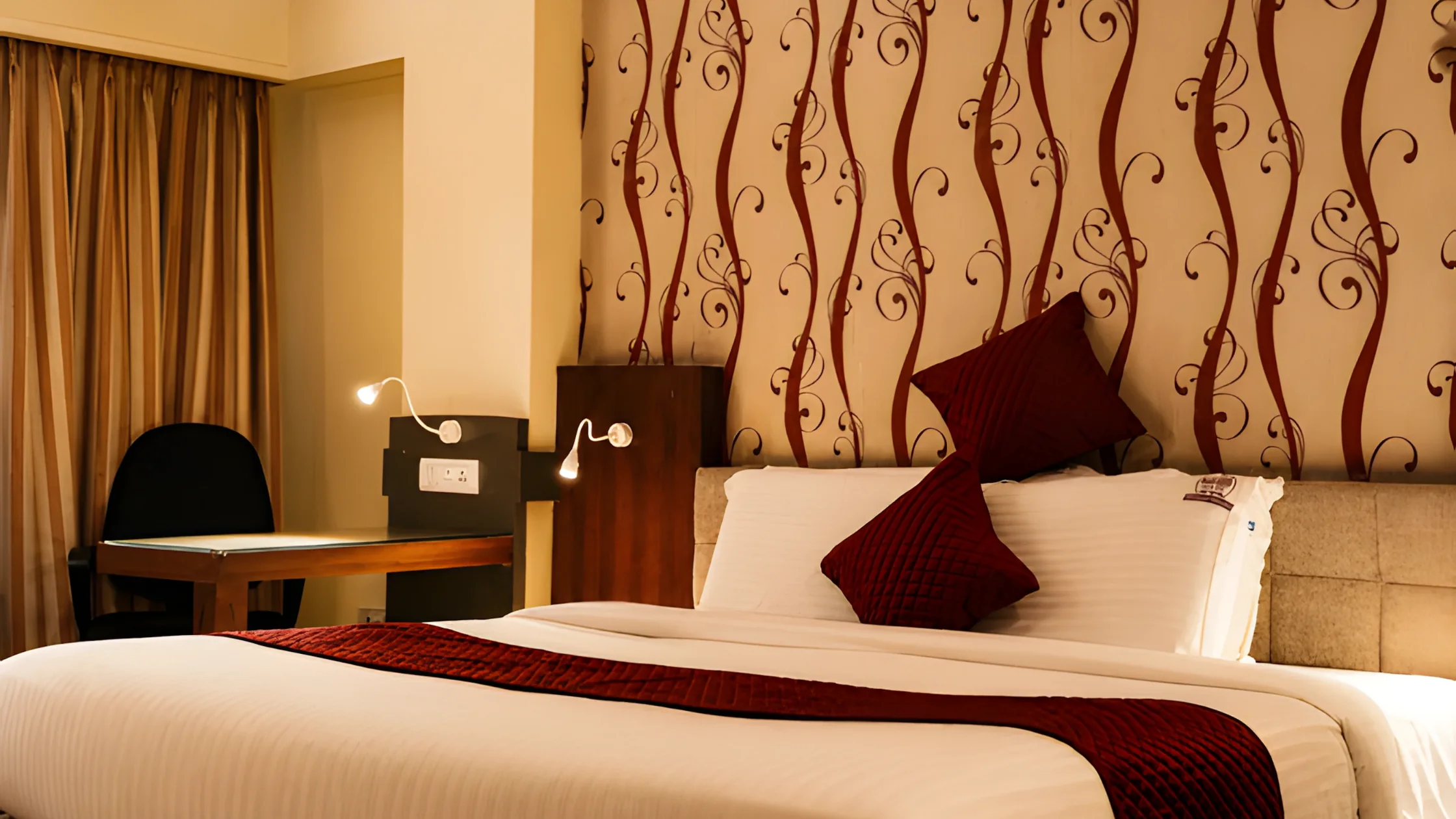 Comfortable hotel room in Mysore with a double bed, decorative wallpaper, and bedside reading lights.