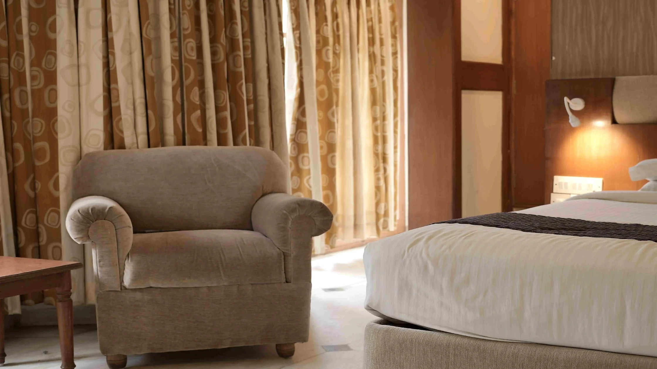 Comfortable hotel room with a cozy armchair, clean bedding, and warm lighting in Mysore.