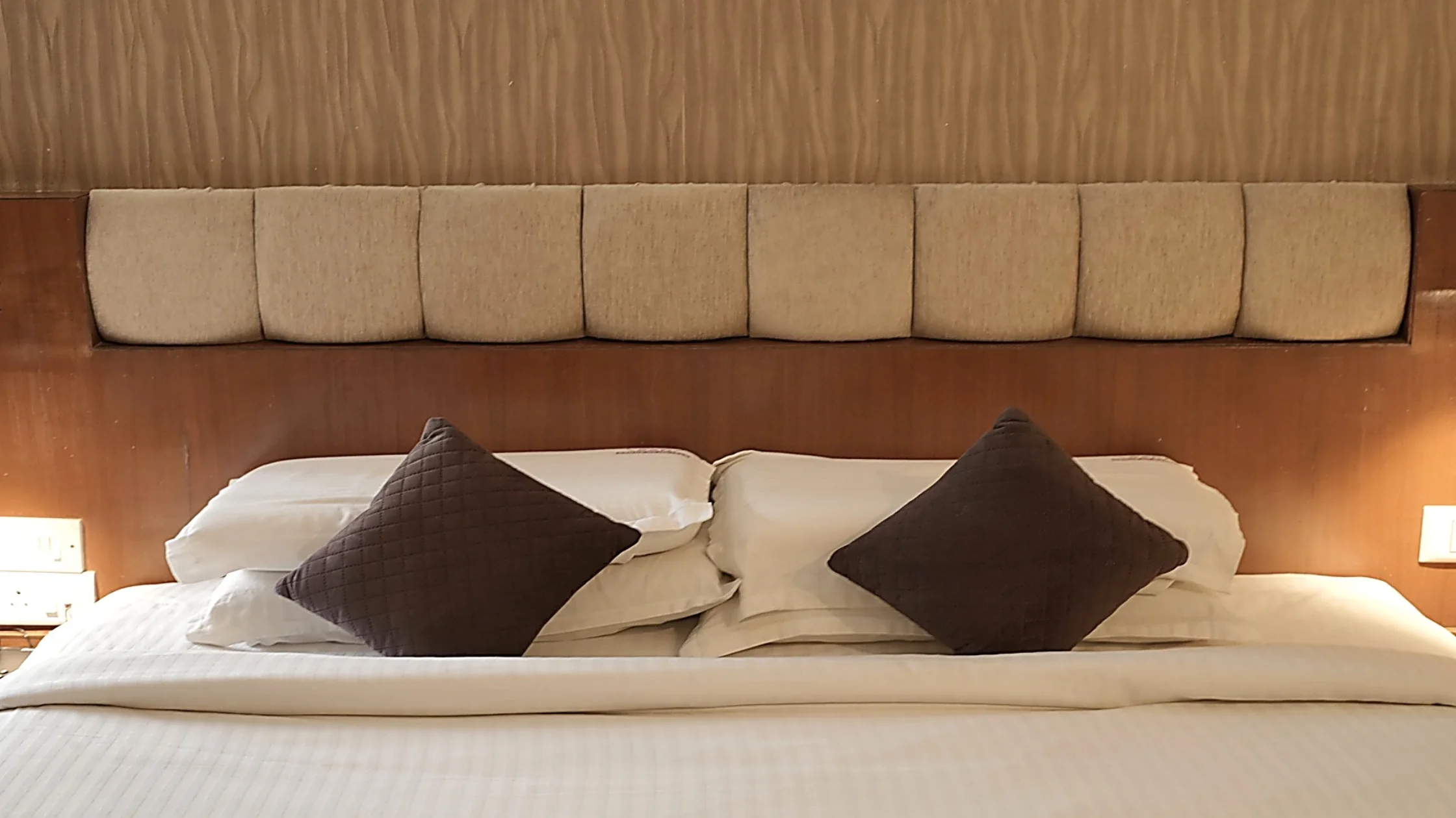 Comfortable hotel bed in Mysore with clean white linens, soft pillows, and a cushioned wooden headboard.