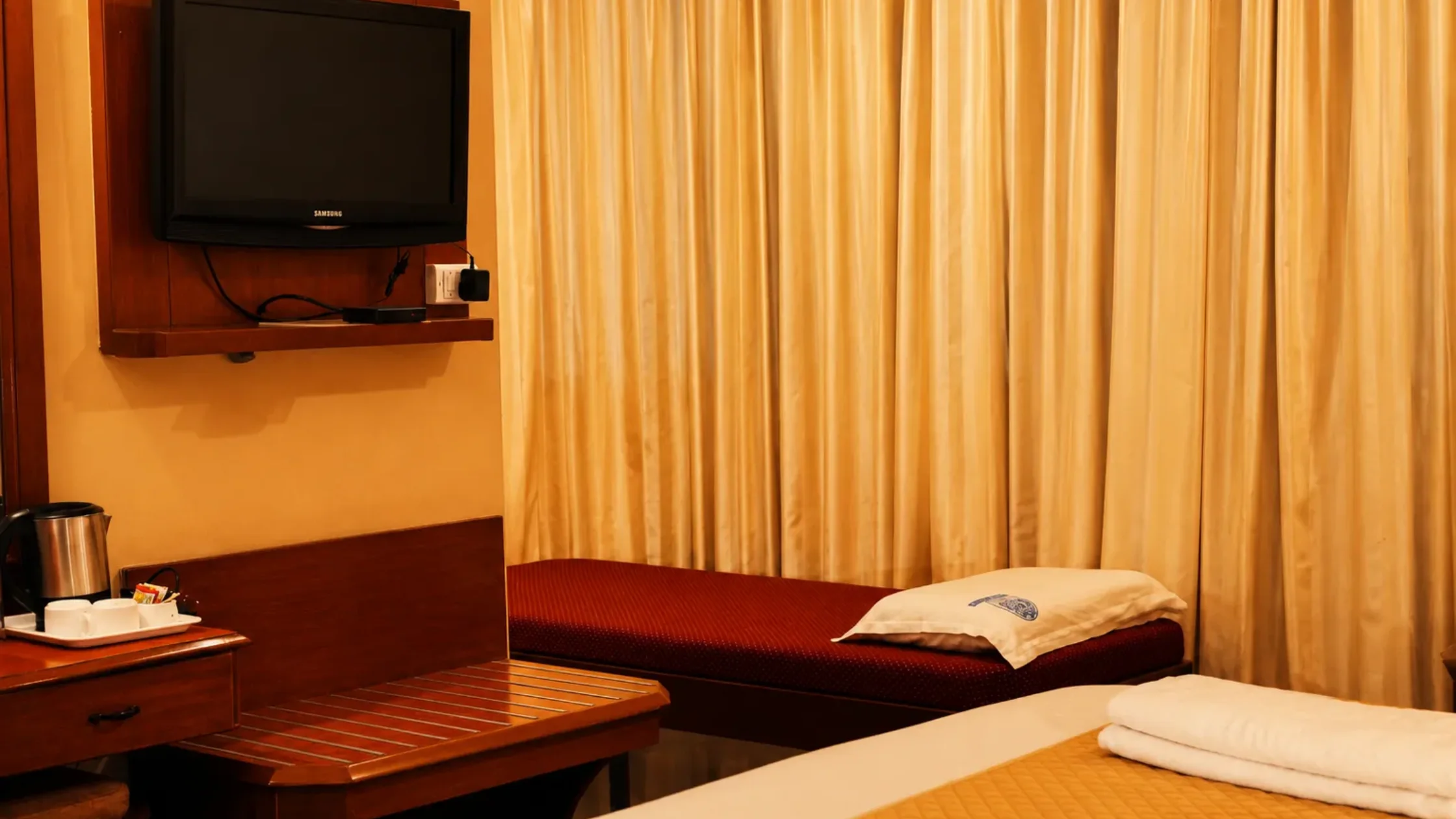Hotel room in Mysore with twin beds, a television, curtains, and a tea-making station for a comfortable stay.