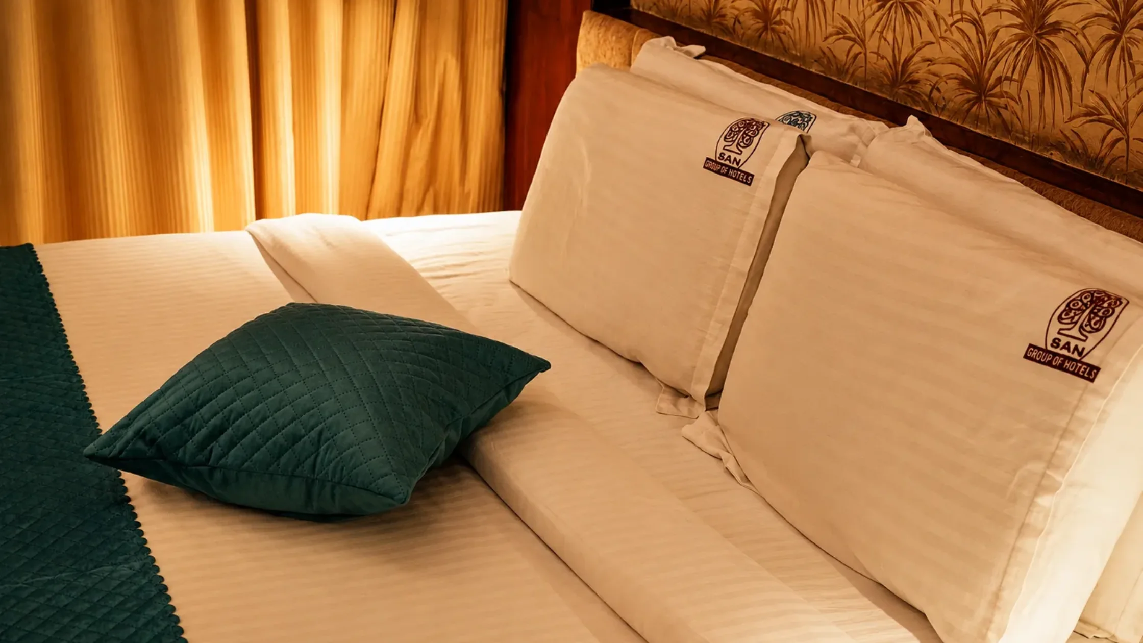 Comfortable hotel bed at SAN Group of Hotels with clean bedding and warm lighting.